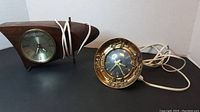 Two clocks together: a wooden Mid-Century Modern Westclox and a small round gold-tone Gilbert Clock Corp clock, both with attached cords