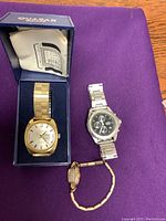 Photo of three watches on purple cloth, including a boxed men's Tradition W watch, a Timex chronograph watch, and a small ladies' watch