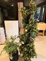 Artificial trailing vine plant wrapping around a vertical support, placed in a black pot on floor