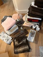 Photo showing multiple folded towels in brown, white, beige, red, and pink colors along with vanity accessories and makeup mirror on floor