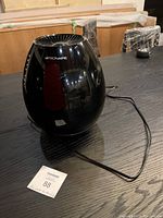 Photo shows a glossy black Bionaire air purifier on a dark wood table with power cord extended. The unit is oval shaped with top vents for airflow.