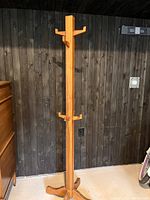 Full coat tree standing against wooden wall, showing its height and base