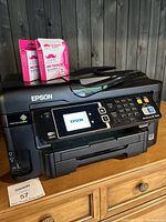 Epson printer front showing LCD display and ink tank compartments, with two pink ink cartridges on top.