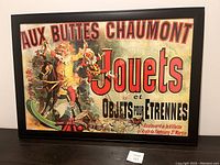 Photo of the framed vintage poster 'Aux Buttes Chaumont' with colorful illustration and bold French text in a black wood frame.