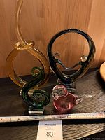 Four decorative glass sculptures shown together on wooden surface with ruler indicating size