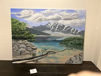 Front view of the landscape painting showing mountains, lake, rocks, and trees on a canvas.