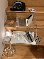 Wide view of entire lot showing Wii console, Balance Board, wheel controller, sensor bar, cables, wrist straps, carrying case, and game cases on stairs.