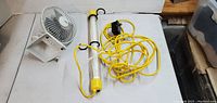 Photo showing a small white electric fan and a yellow portable work light with long power cord