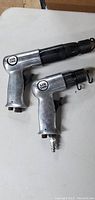 Two pneumatic air tools placed on a white surface, showing metal and black plastic construction with 'Air Tool' label