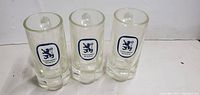 Three clear glass beer mugs standing upright showing the front blue Lowenbrau lion logo