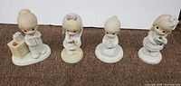 Front view showing all four 6-inch Precious Moments figurines arranged side by side on a brown surface.