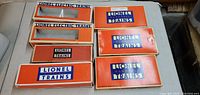 Photo shows seven vintage Lionel train boxes in varying sizes and styles on a white surface, arranged in a group for viewing.