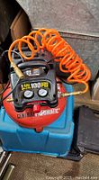 Front and top view showing the air compressor tank, gauges, pressure knob, and attached orange coiled air hose.