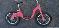 Side view photo showing pink Kazam youth balance bike with black seat and tires, silver spokes and rims