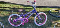 Side view of purple and pink Huffy Sea Stars children's bicycle with white 20 inch tires on grass outdoors.