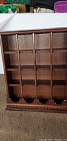 Front view of wooden wall-mounted display shelf showing four vertical compartments with semicircular cutouts at bottom and decorative carved base molding.