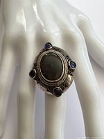 Front view of the chunky sterling silver ring with large labradorite center stone surrounded by four dark purple amethyst stones on a white mannequin hand.