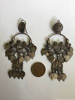 Front view of large silver dangle earrings with two love birds and multiple dangling leaf charms. Includes a coin for size comparison showing 8 cm by 4 cm approximate dimensions.