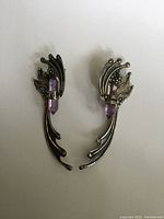 Front view of pair of sterling silver wing-shaped earrings with purple amethyst crystals.