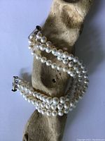 Triple strand pearl bracelet coiled on a piece of wood showing pearls and clasp.