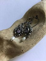 Pair of sterling silver earrings with marquise shaped amethyst stones and small pearl drops, shown on a wooden background.