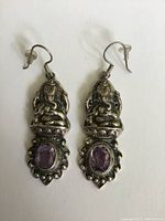 Pair of vintage sterling silver earrings featuring detailed Thai Buddha design with oval amethyst gemstones, shown on a white background.