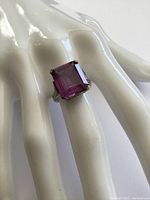 Close-up photo of vintage sterling silver ring with large square-cut amethyst glass stone worn on a display hand.
