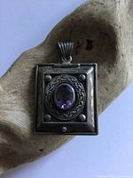 Front view of square sterling silver locket pendant with oval amethyst center stone, showing tarnish and detailed design.
