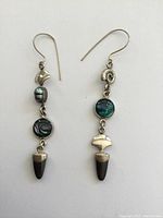 Pair of dangle earrings with sterling silver, abalone stones, and dark tapered stones laid flat on white background.