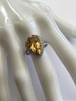 Front angled view of the sterling silver ring showcasing the pear-shaped citrine gemstone surrounded by clear stones on a hand stand.