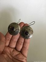 Both sterling silver round etched earrings held in hand showing front view with garnet cabochons and etched pattern detail.