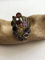 Close-up view of the sterling silver cluster ring showing assorted colored gemstones including peridot, garnet, amethyst, citrine, and topaz in various cuts and sizes arranged on the broad ring face.