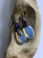 Close up front view of the sterling silver earrings showing the moonstone style drop and amethyst stone on a wood holder.