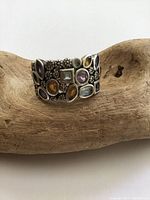 Front view of a wide sterling silver ring with multiple colorful gemstones in various shapes set in textured silver beads.
