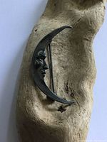 Front view of the crescent moon brooch showing detailed face profile on textured background.