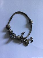 Sterling silver Pandora charm bracelet laid flat showing various charms including filigree bead, heart charms, bird charm, and dangling heart umbrella charm