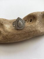 Front view of sterling silver pear-shaped diamond cluster ring on natural wood display showing teardrop shape with multiple small stones.