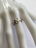 Ring worn on white mannequin hand showing the three colorful gemstones (topaz, amethyst, peridot) set in a sterling silver band.