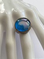 Close up of tarnished sterling silver ring with blue round glass cabochon showing iridescence and surface marks.