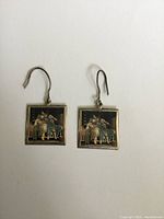 Pair of square sterling silver dangle earrings each featuring a painted image of a mother and daughter playing banjo against dark background. Earrings measure about 2 cm square excluding hooks.