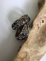 Pair of silver hoop earrings with organic Brutalist style texturing and central round garnet cabochons, sitting on light wood background.