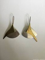 Pair of dangle earrings on white background, showing front view of overlapping brass and silver geometric shapes