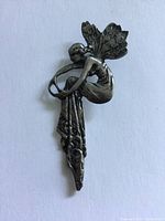 Close-up photo of the vintage sterling silver fairy pendant showing the seated fairy with wings and ornamental details, highlighting the tarnished surface and wear.