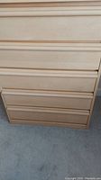 Front view of the light wood chest of drawers showing integrated handles on six drawers, with visible surface wear.