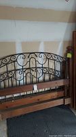 Photo showing metal headboard with scroll pattern framed in wood, part of bed frame.