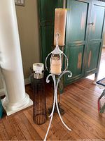 Three pillar candle holders of varying sizes and styles displayed on hardwood floor near green cabinet and architectural column with pillar candles on each.