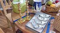 Photo showing two Baldwin brass candlesticks and boxed set of four Crate and Barrel fish-shaped aluminum tea light candle holders on a wooden table.
