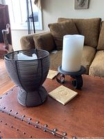 Side view of two candle holders with white candles and two ceramic coasters on wooden table in living room.