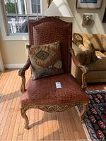 Front view of brown leather armchair with ornate carved wooden legs and arms, displaying decorative nailhead trim and textured leather upholstery.