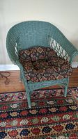 Front view of green painted wicker chair with floral cushion on a patterned rug.